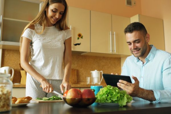 Couple preparing food and using tablet in kitchen.